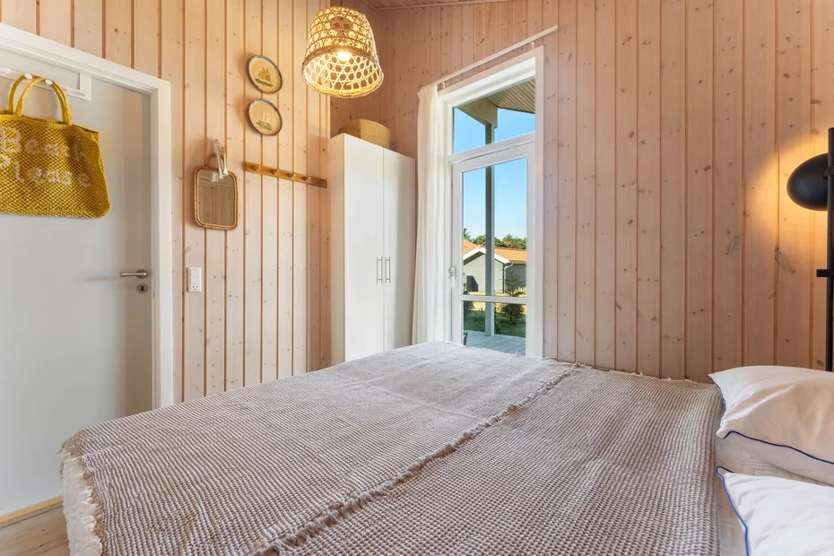 A bedroom with a bed, a white wardrobe, and a tall window.