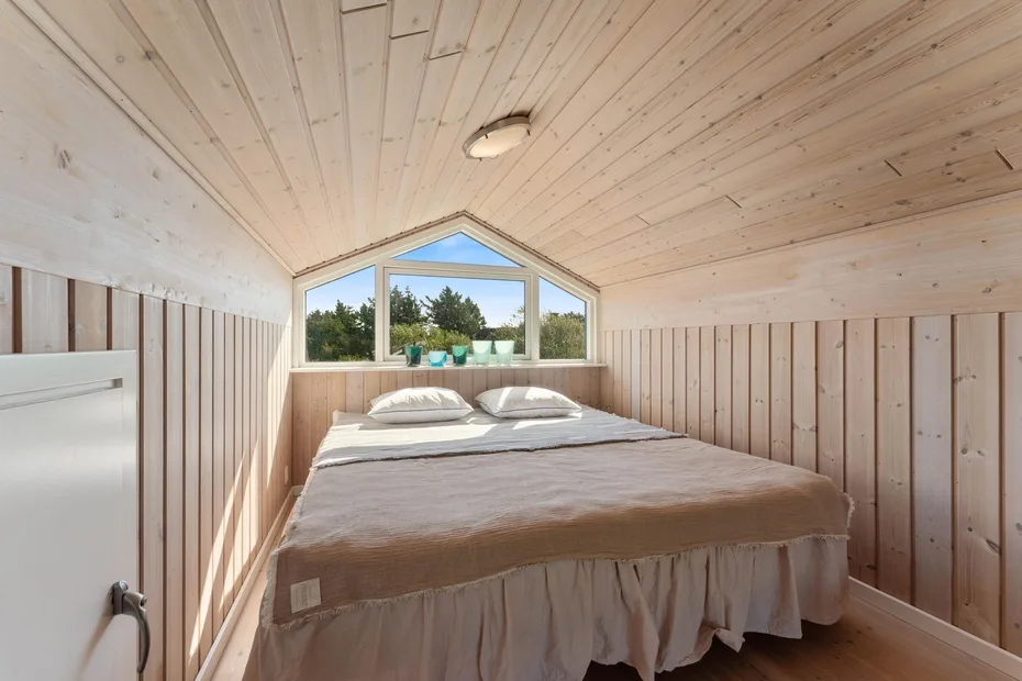 A compact bedroom with a bed beneath a peaked window.