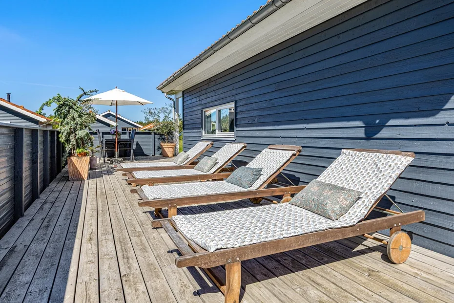 A wooden deck beside a dark-sided building has several loungers and a patio umbrella.