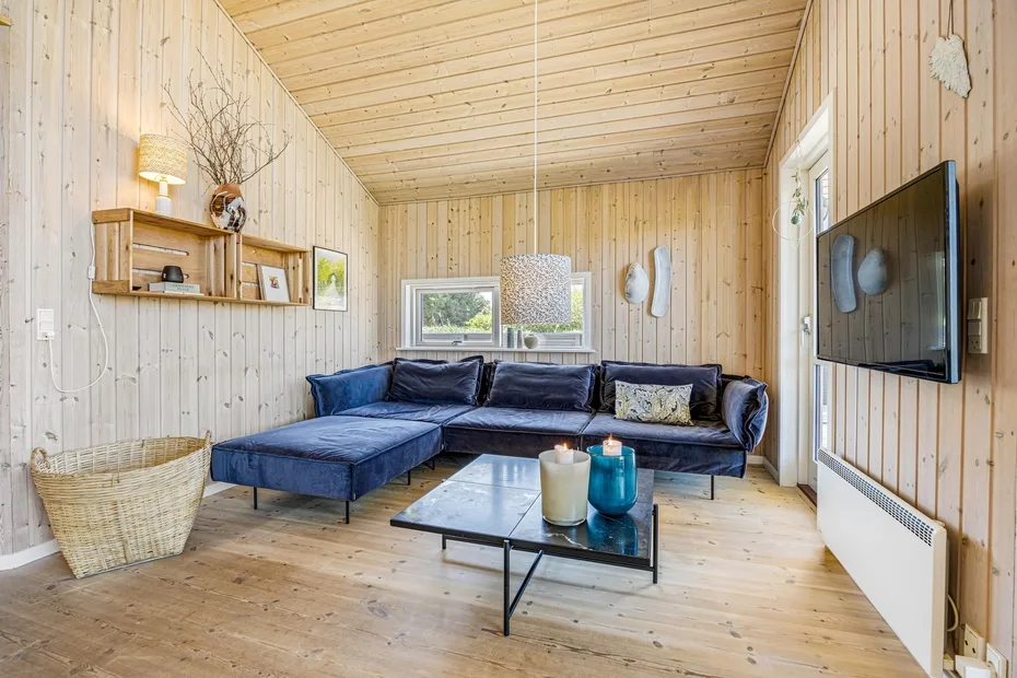 Una sala revestida de madera con un sofá seccional oscuro y una mesa de centro de vidrio.