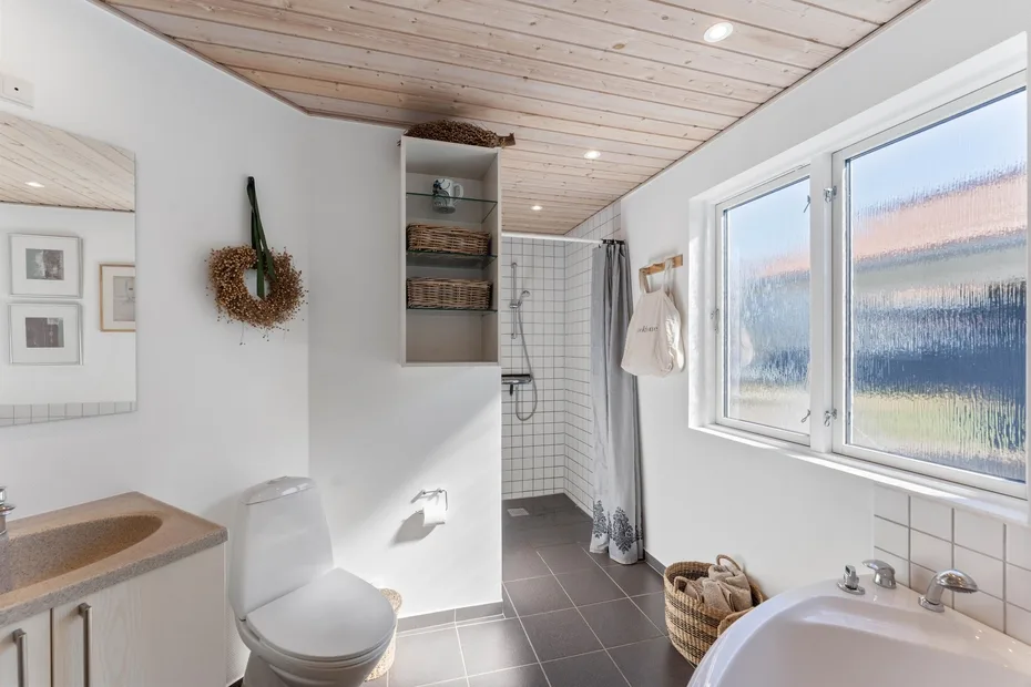 A bright bathroom with a tiled shower, toilet, and large windows.
