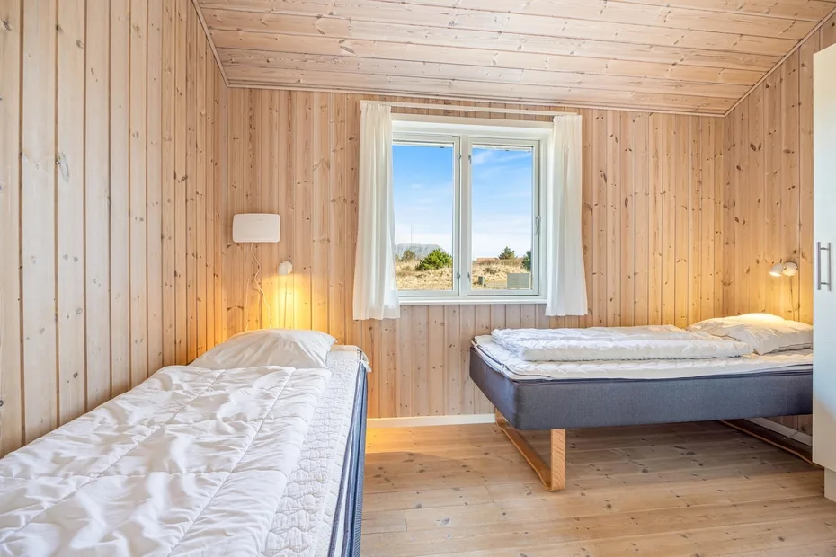 A wood-paneled bedroom with two beds and a window overlooking the landscape.
