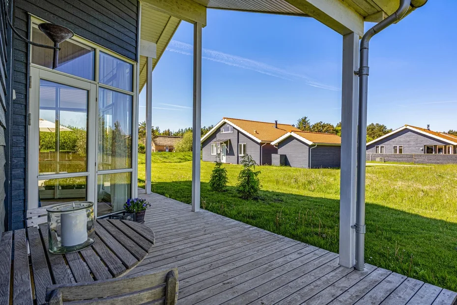 A covered wooden deck overlooks a grassy field and neighboring houses.