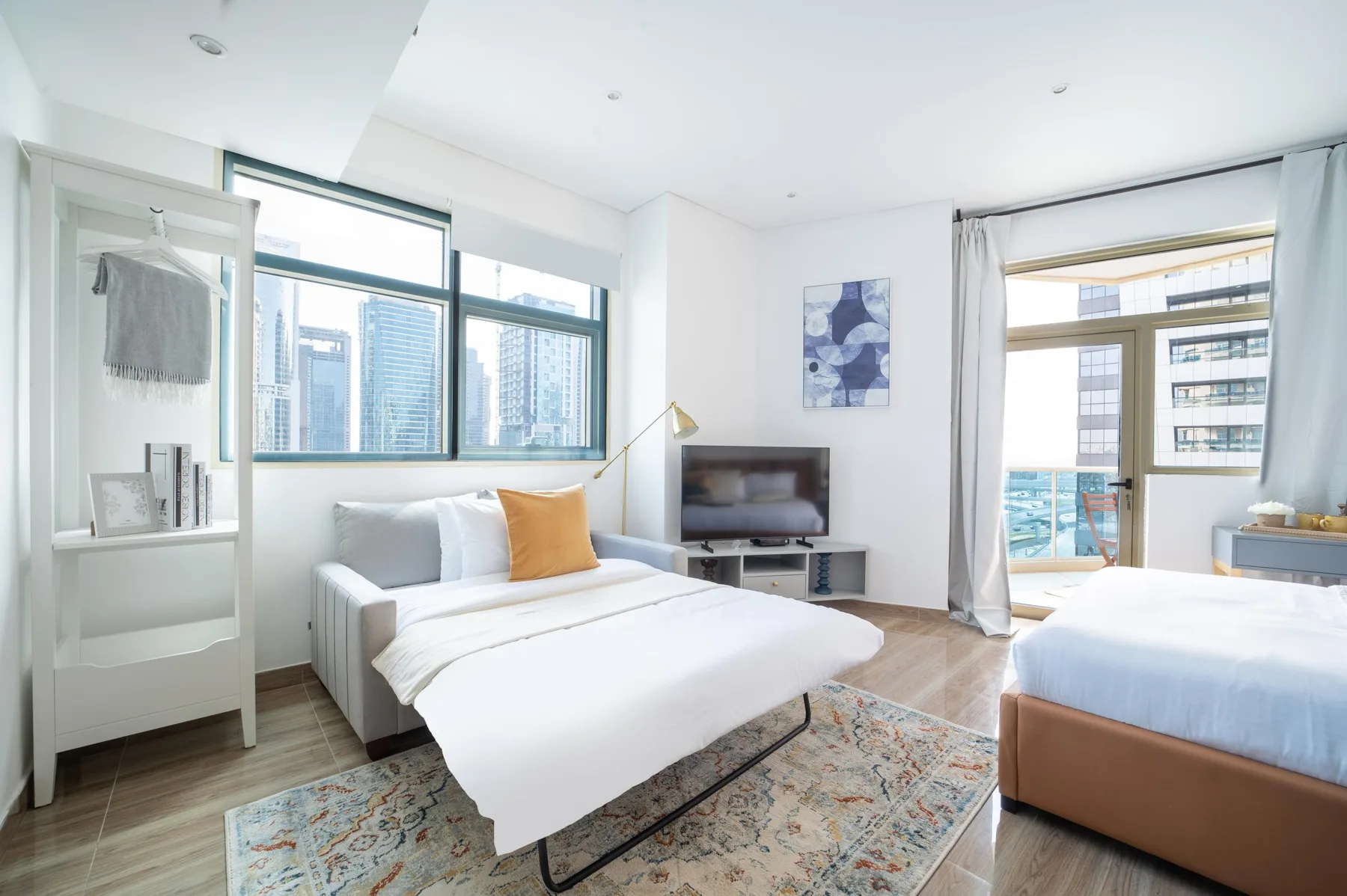 Un dormitorio luminoso con dos camas, ventanas grandes y un televisor.