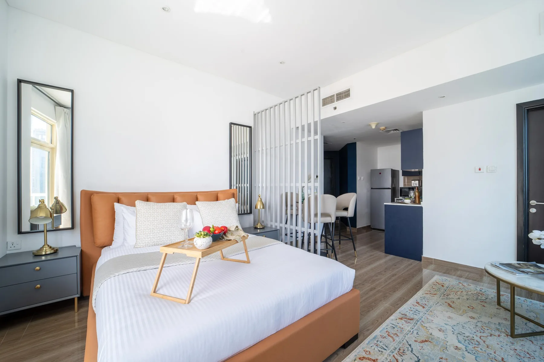 Un dormitorio luminoso con una cama grande y una cocina abierta al fondo.