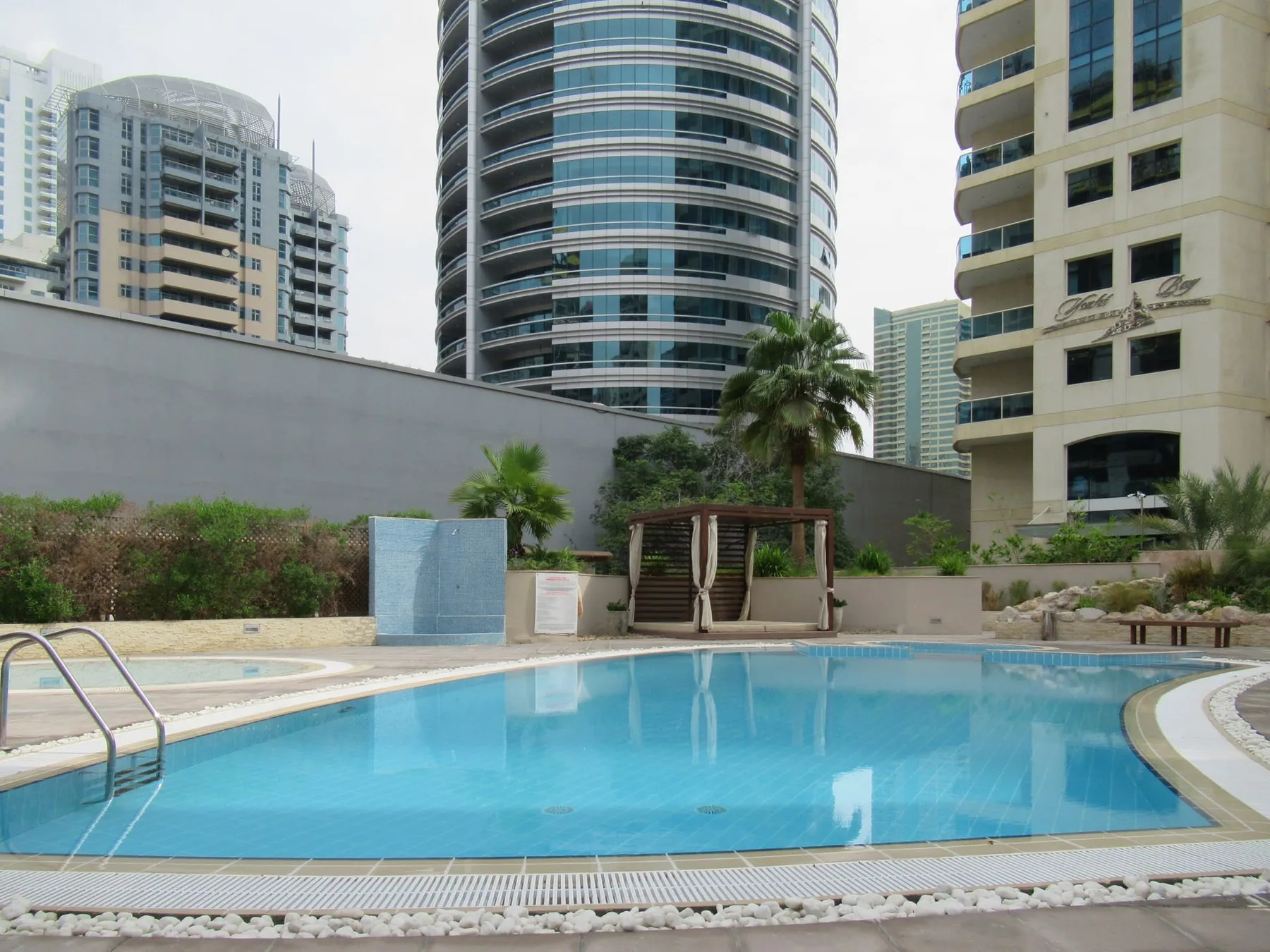 Una piscina está frente a un patio ajardinado y varios edificios altos.
