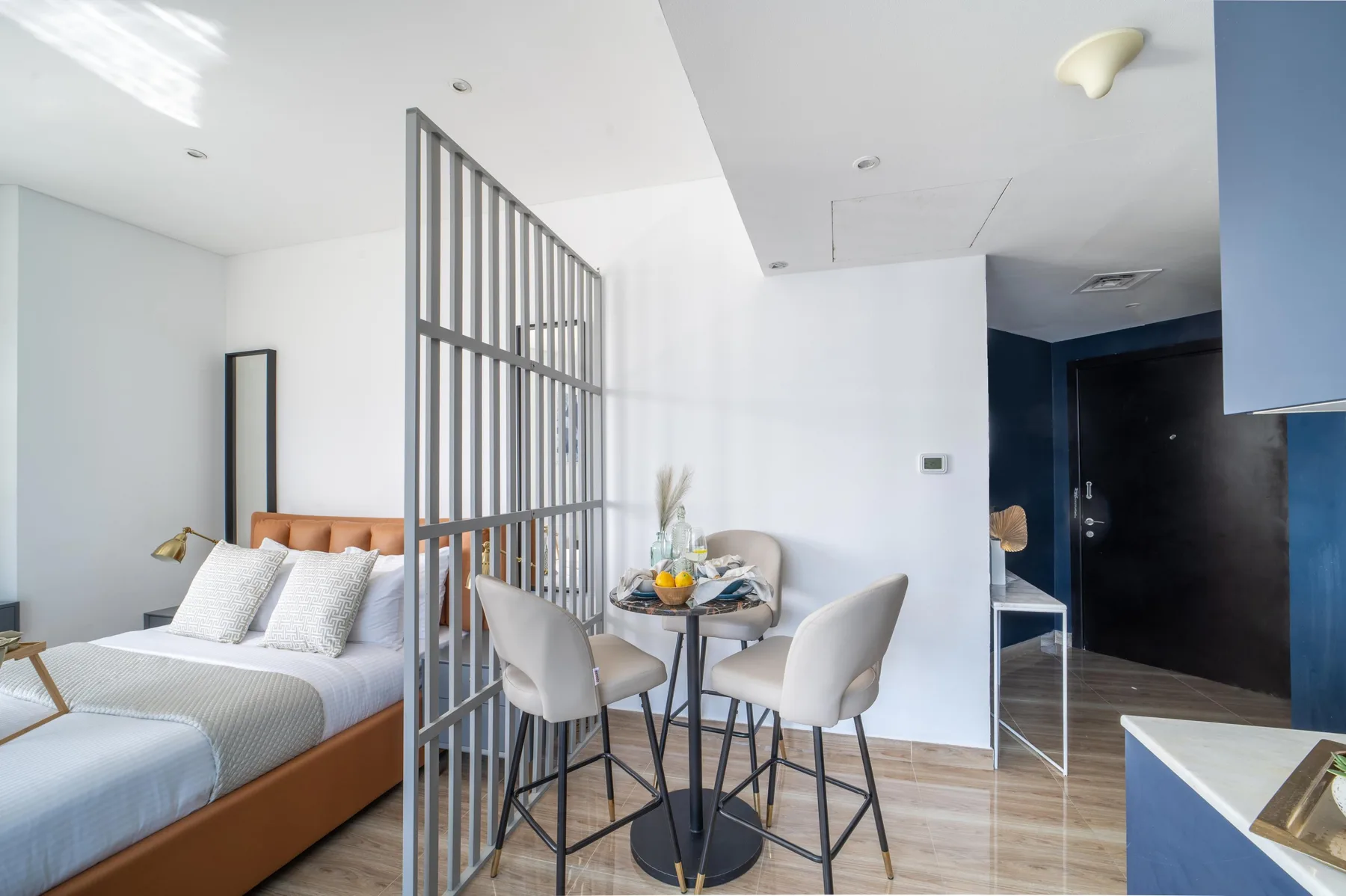 Un dormitorio y una zona de comedor comparten un espacio abierto, separados por una división de listones metálicos.