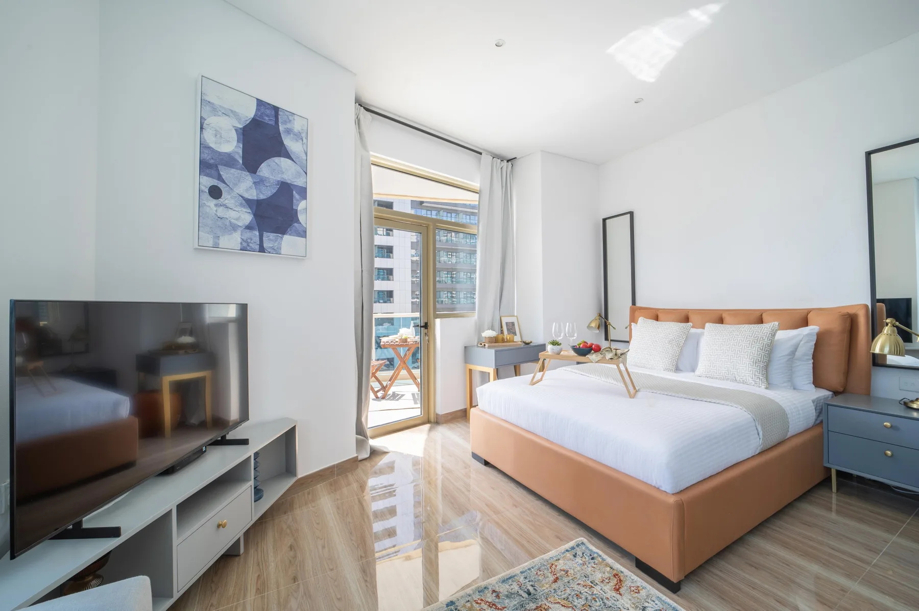 Un dormitorio luminoso con una cama, un televisor y puertas de vidrio que dan a un balcón.