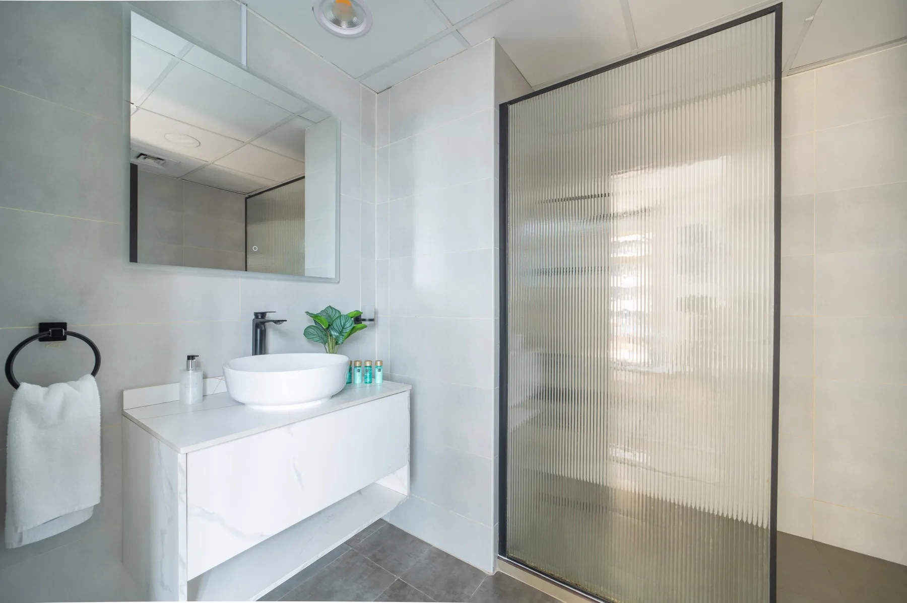 Un baño luminoso con lavabo blanco y una mampara de vidrio para la ducha.