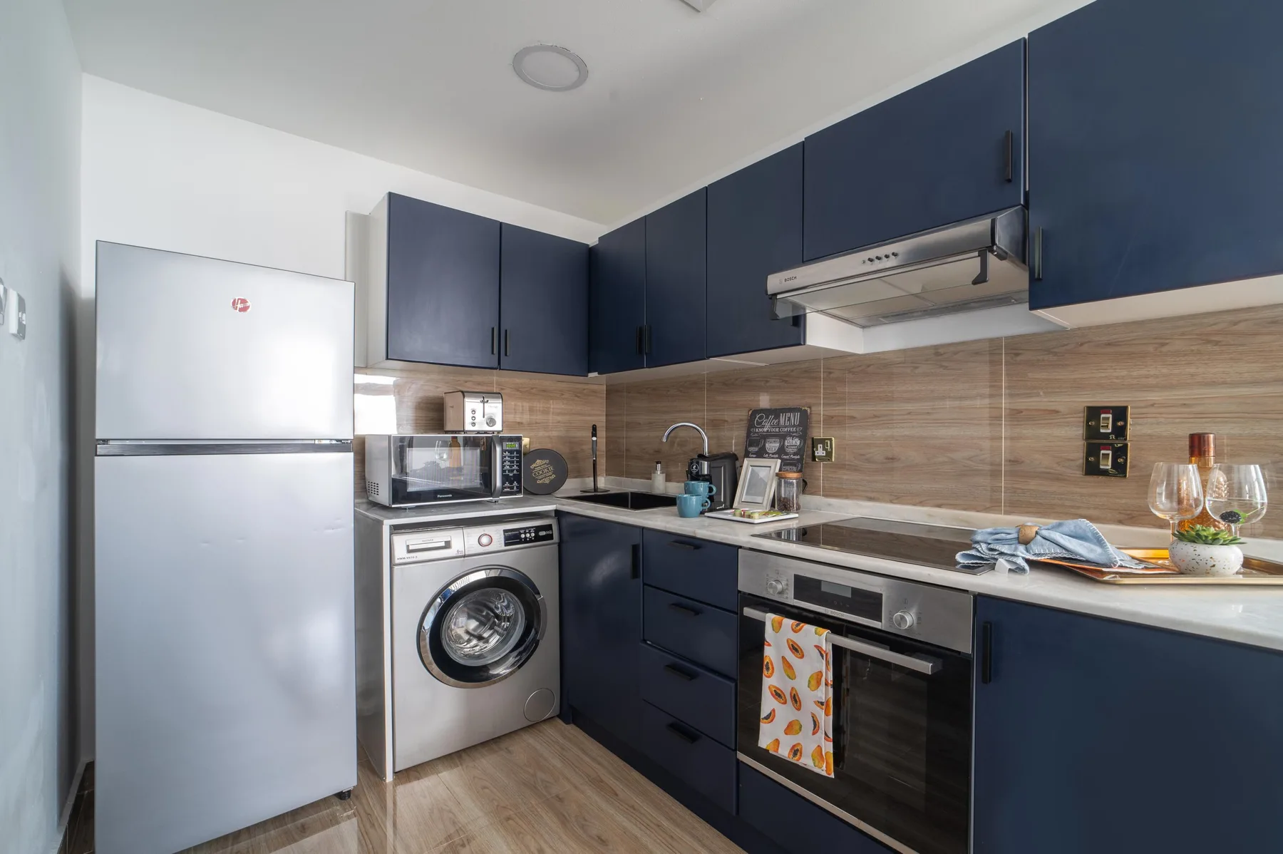Una cocina compacta con gabinetes oscuros, un refrigerador y electrodomésticos.
