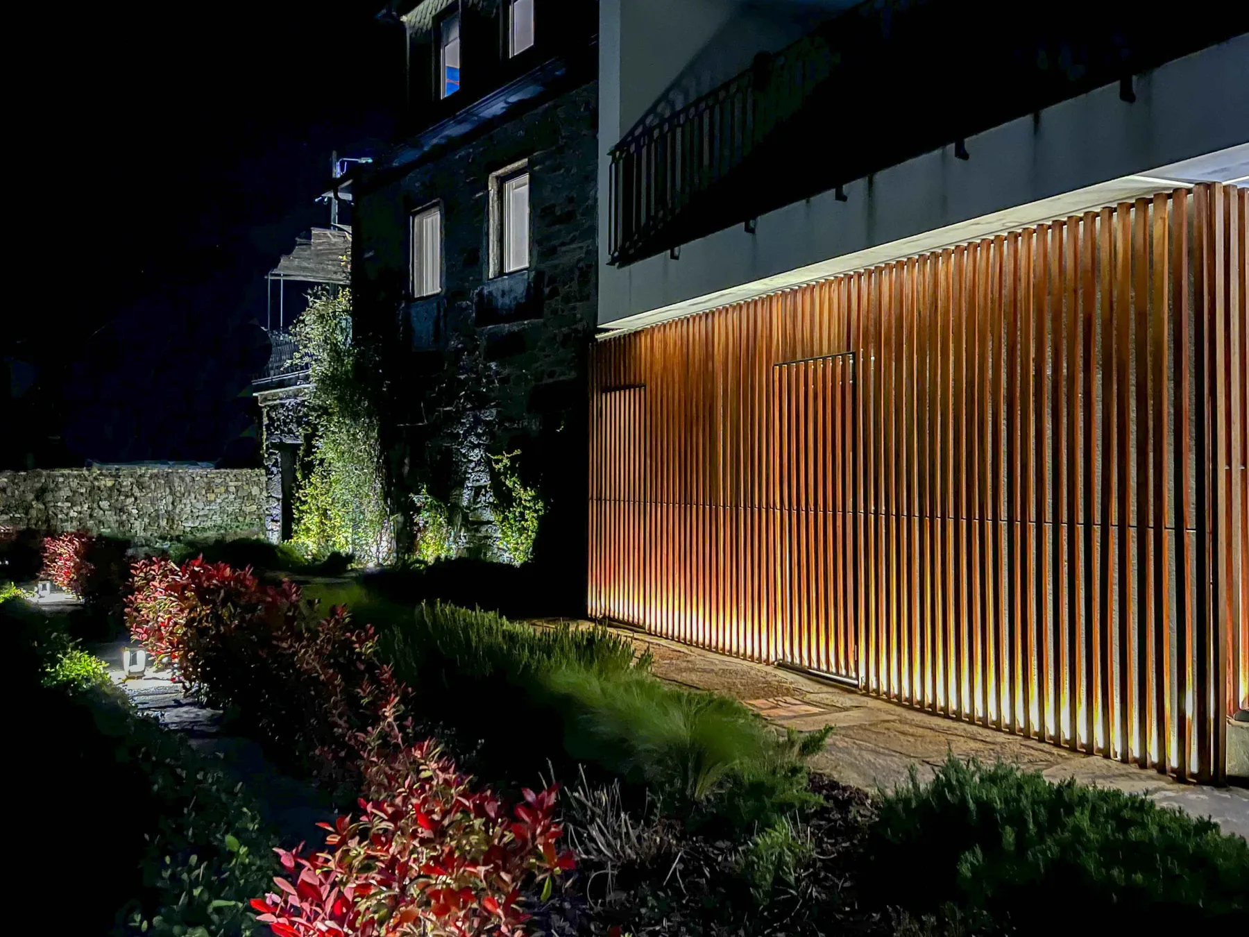 Exterior de un edificio moderno por la noche, con una alta celosía iluminada junto al sendero.