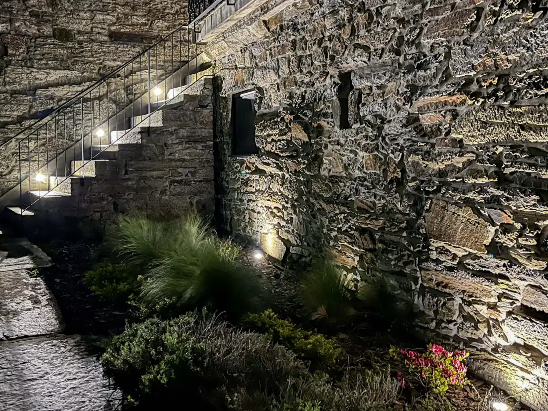 Un patio de piedra con escaleras iluminadas y parterres con plantas.