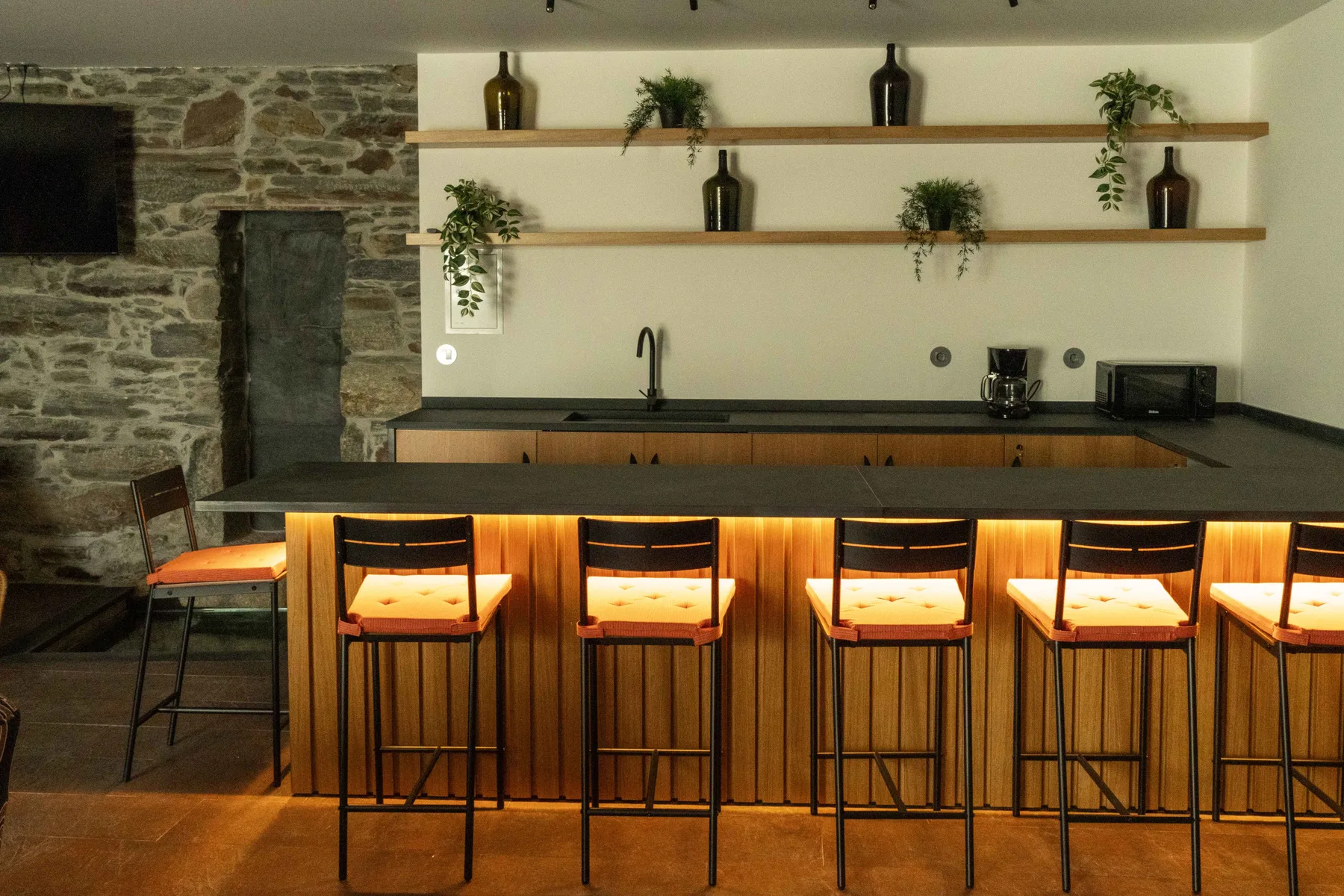 Una cocina con una barra larga y asientos debajo de estantes de pared.