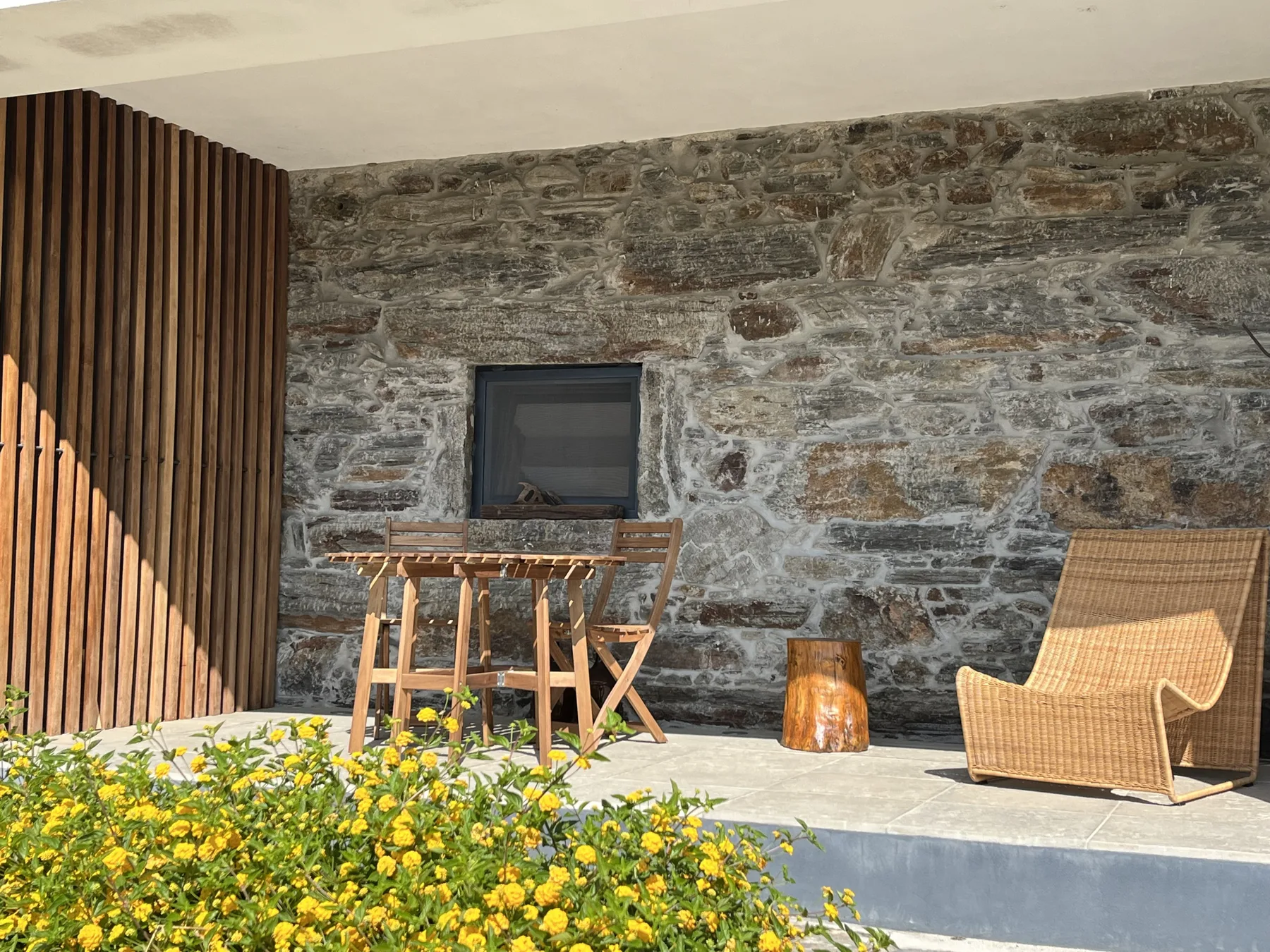 Un patio con paredes de piedra, asientos de madera y un jardín de flores amarillas.