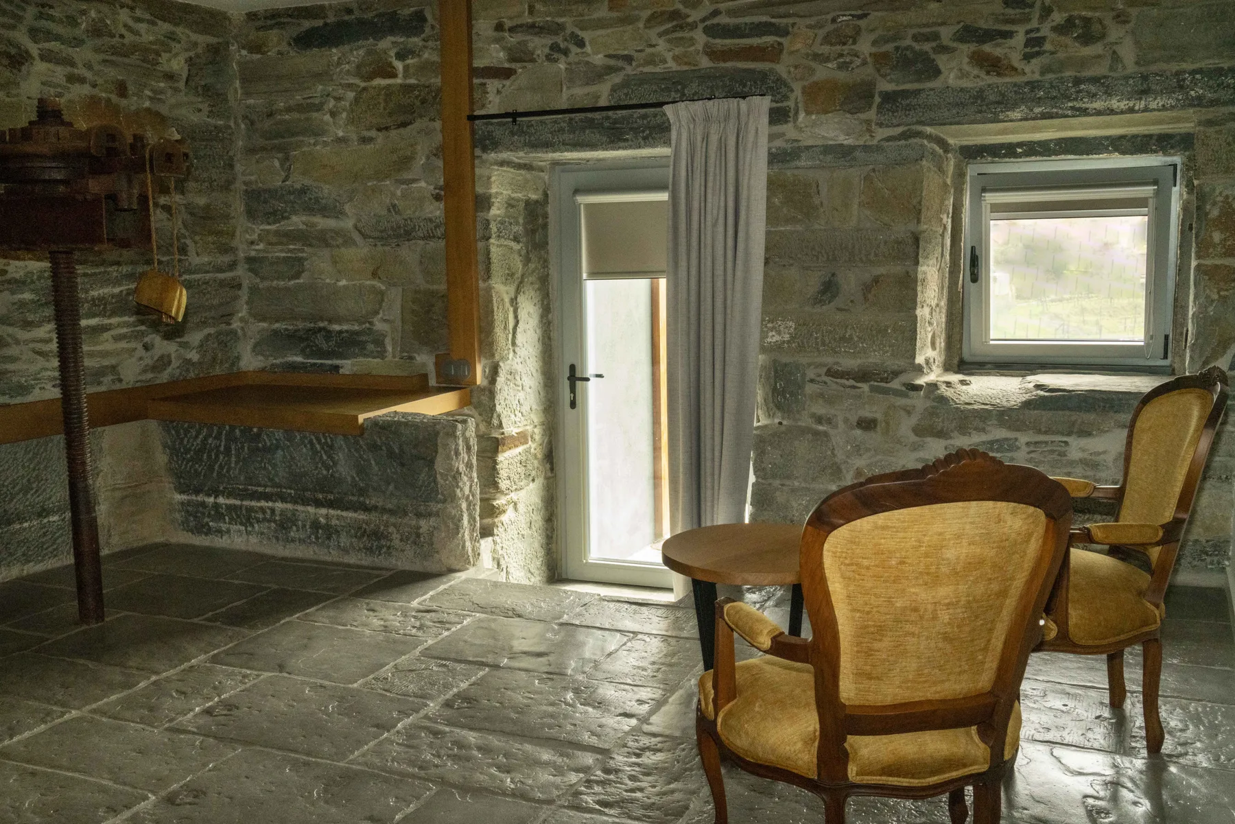 Una habitación de piedra con una mesa y asientos tapizados junto a dos ventanas.