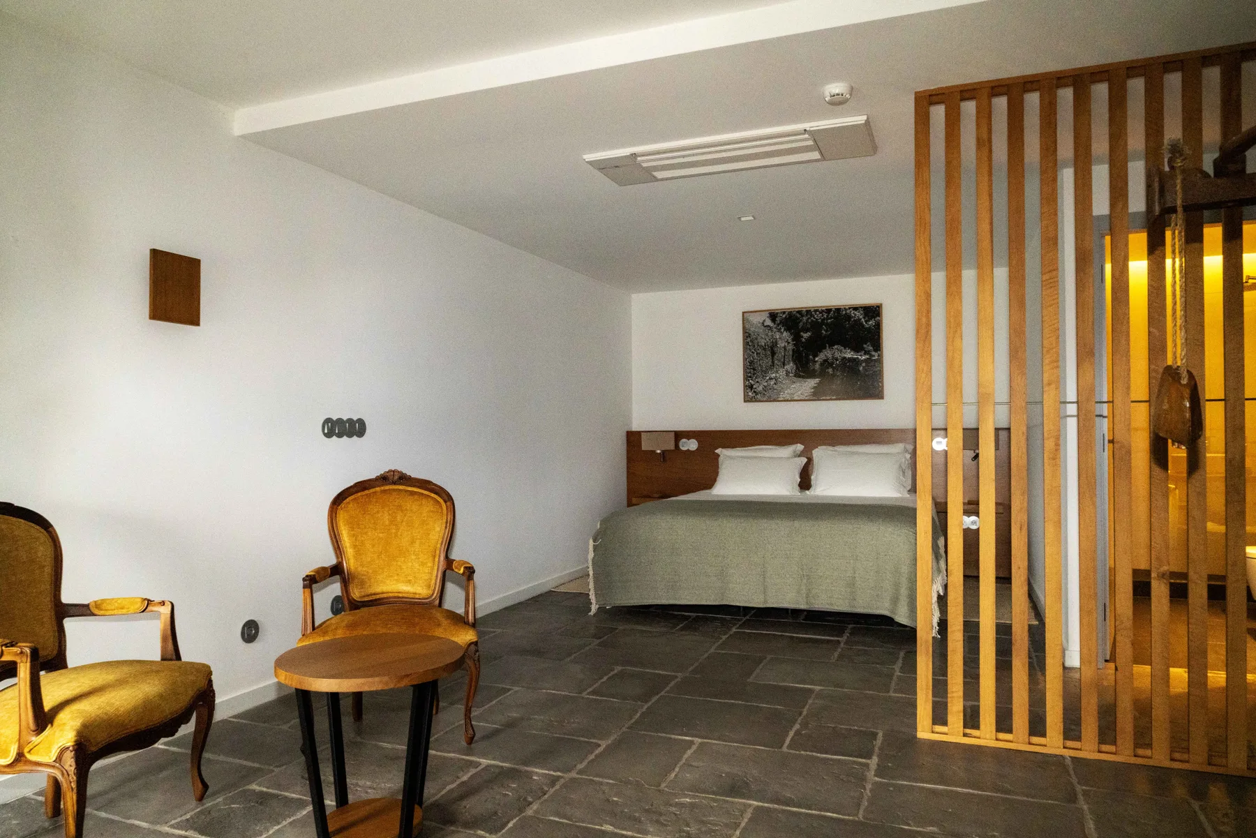 Un dormitorio con una cama, una obra enmarcada y un separador de listones de madera.