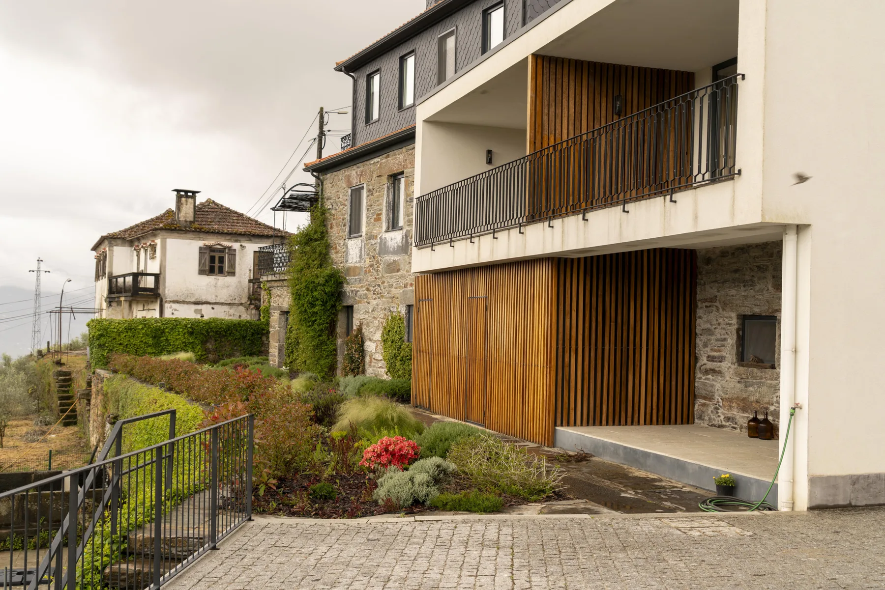 Un edificio moderno con listones de madera se encuentra junto a una casa antigua de piedra.