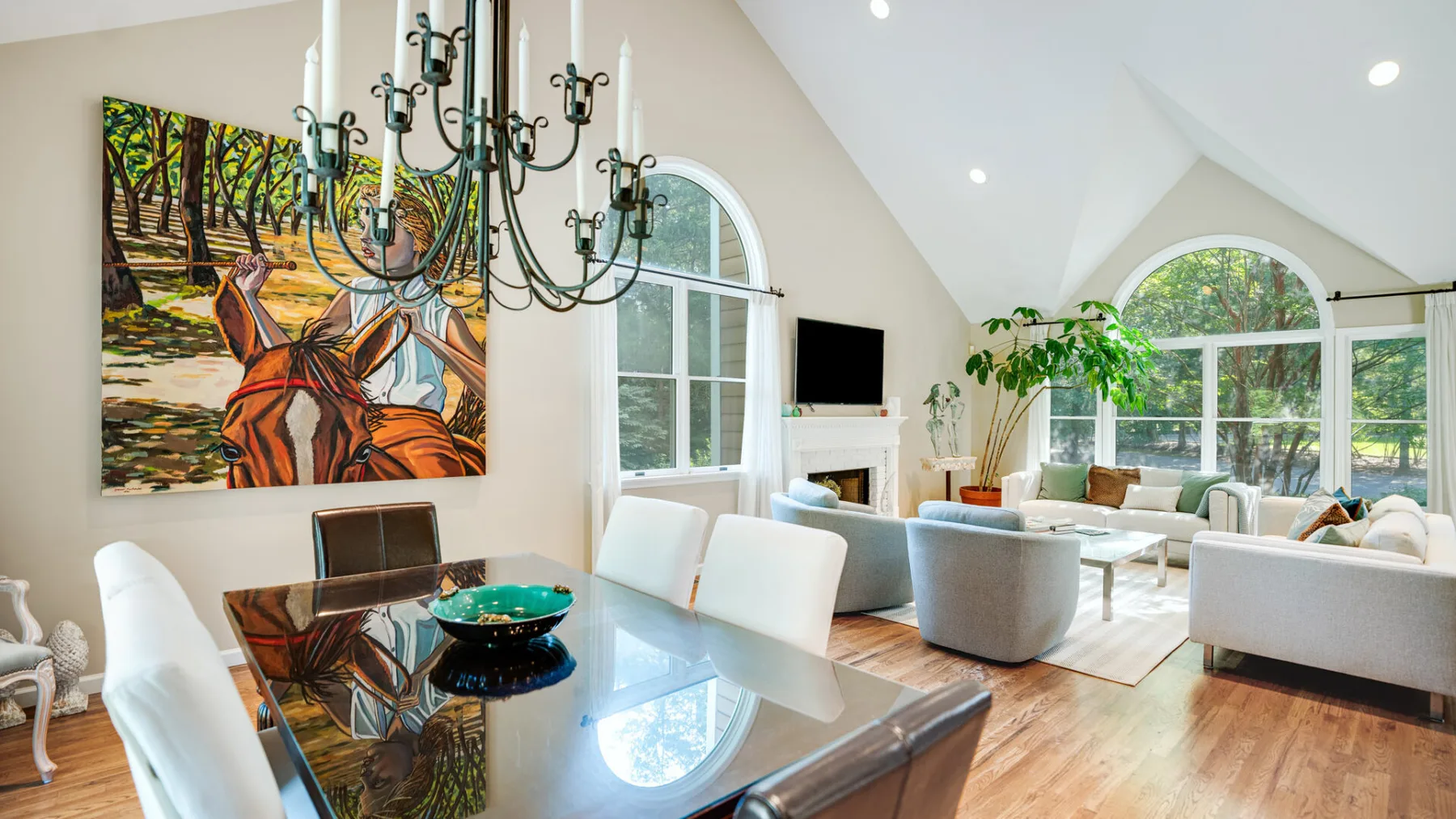 Una luminosa sala de estar y comedor con ventanas arqueadas y una mesa de comedor de vidrio.