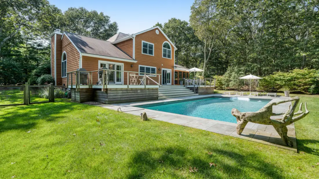 Una casa con piscina y césped en un entorno exterior arbolado.
