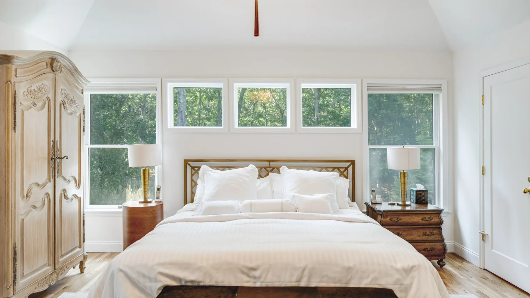 A bright bedroom features a large bed beneath a row of windows.