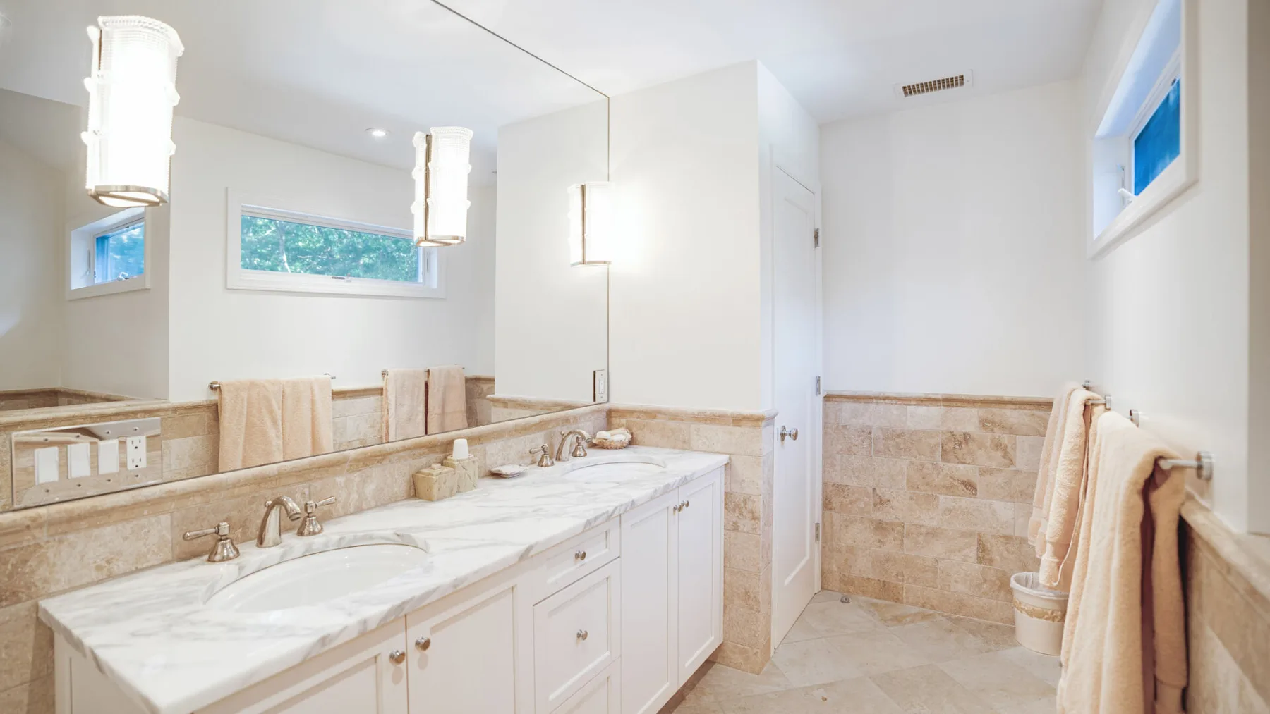 A bright bathroom with a long vanity, mirrors, and a bathtub.