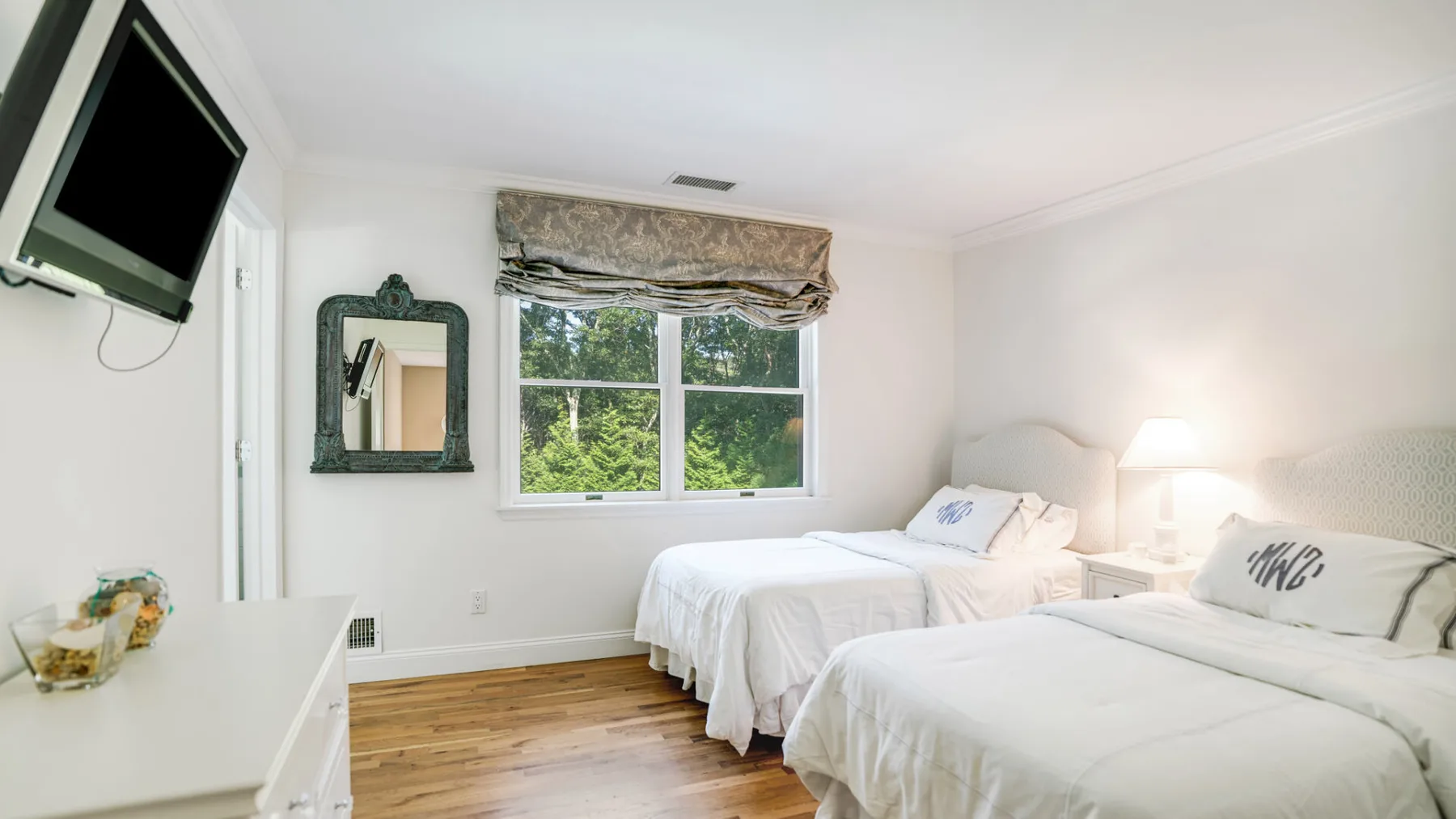 A bright bedroom with two beds, a window, and a television.