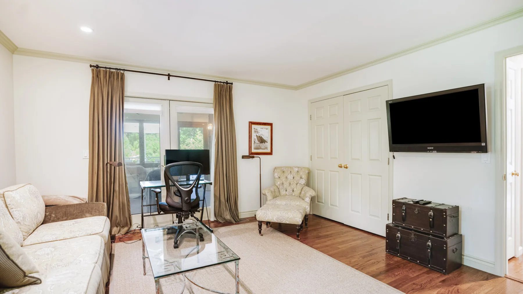 A living room with seating, a glass coffee table, and a television.
