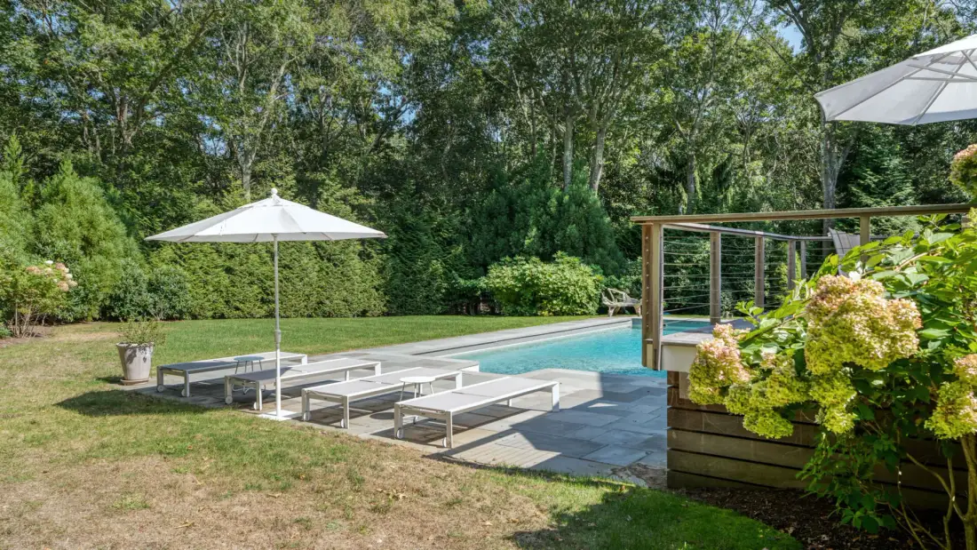 An outdoor swimming pool with a white umbrella and lounge seating beside it.