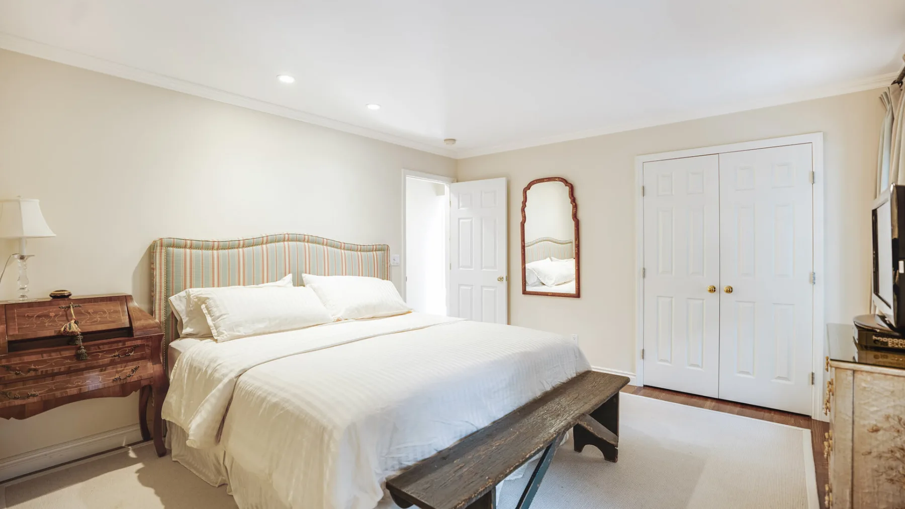 A bedroom with a neatly made bed and a wooden bench at its foot.