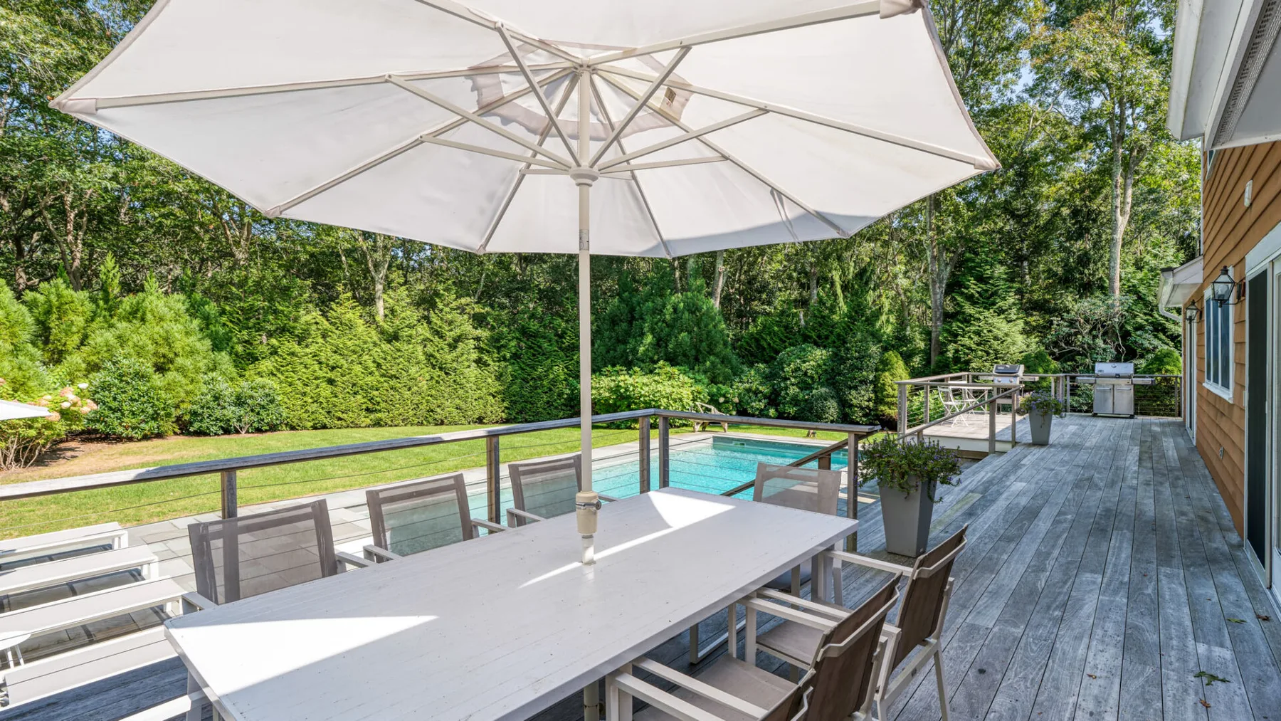 An outdoor dining area beside a swimming pool, shaded by a large umbrella.