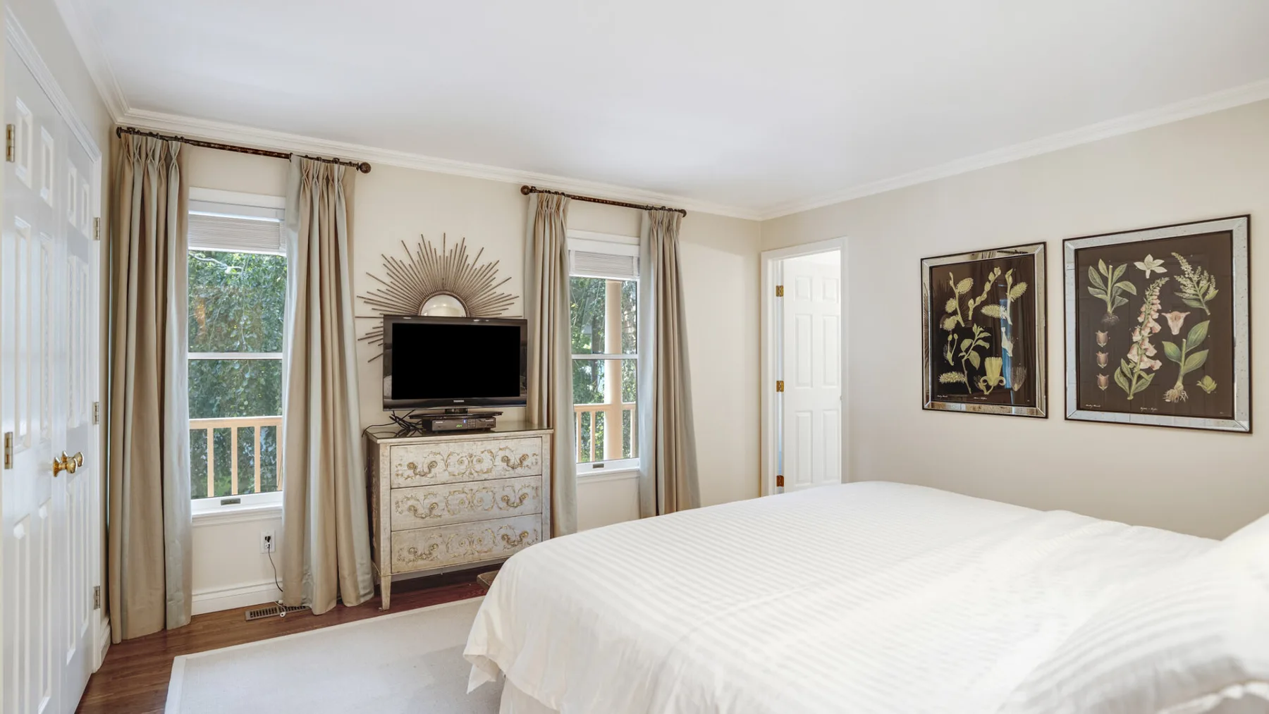 A bedroom with a large bed, a dresser, and framed botanical artwork.