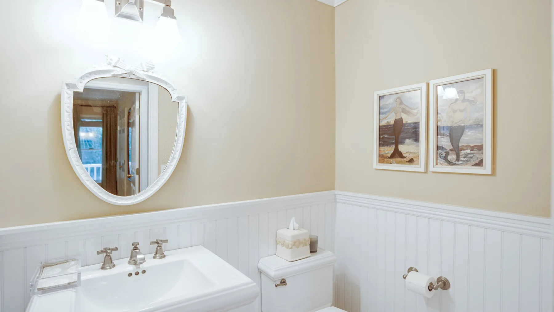 A bathroom with a sink, wall mirror, and framed pictures.