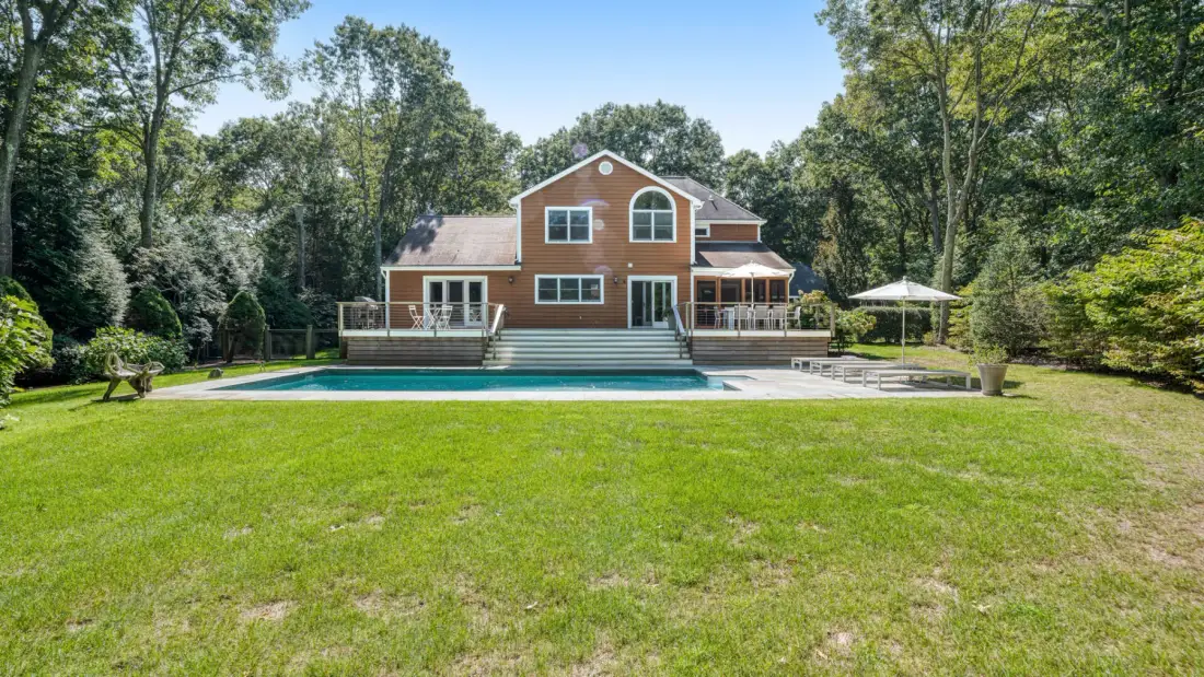 A large house stands behind a swimming pool in a broad grassy yard.