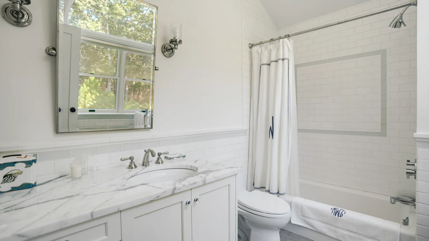 A bright bathroom with a marble vanity, window, and bathtub.