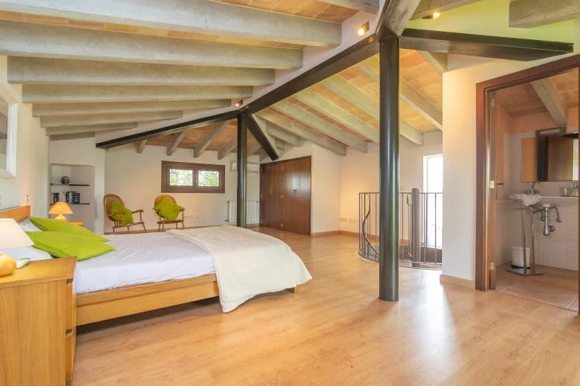 A spacious bedroom with a wooden bed, exposed beams, and an open bathroom doorway.