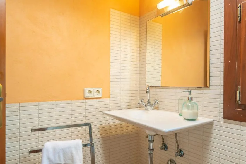 A bathroom with a wall-mounted sink, mirror, and white tiled walls.