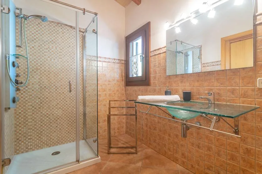 A tiled bathroom with a glass shower and a wall-mounted glass sink counter.