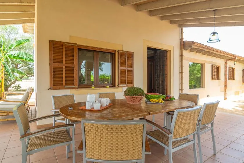 A covered patio dining area with a wooden table and woven chairs.