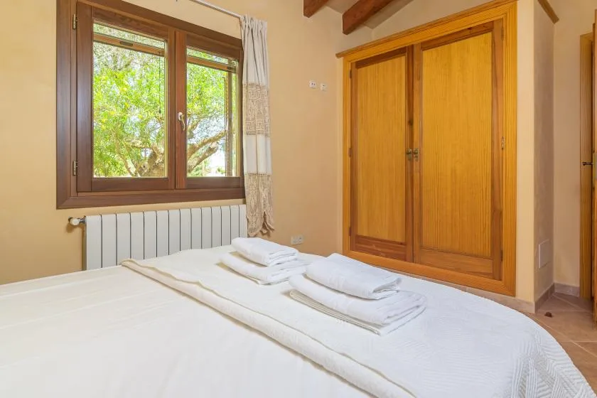 A bedroom with a neatly made bed beneath a window overlooking leafy trees.