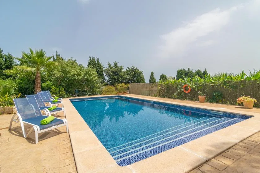 An outdoor swimming pool is surrounded by paved decking and lounge chairs.
