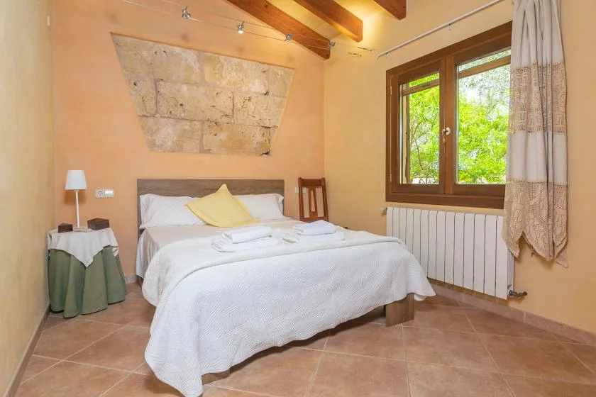 A bedroom with a neatly made bed beneath exposed wooden ceiling beams.