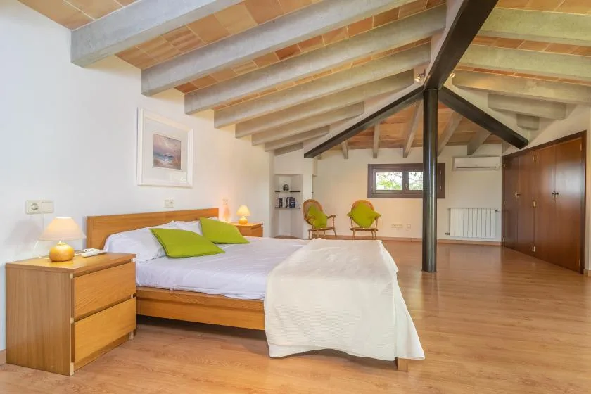 A bedroom with a bed, wooden floors, and exposed ceiling beams.