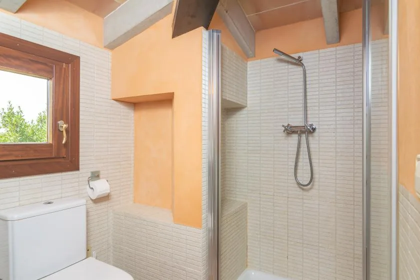 A tiled bathroom with a shower and a wood-framed window.
