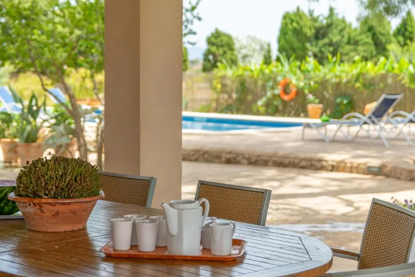 A shaded outdoor dining table overlooks a swimming pool and lounge chairs.