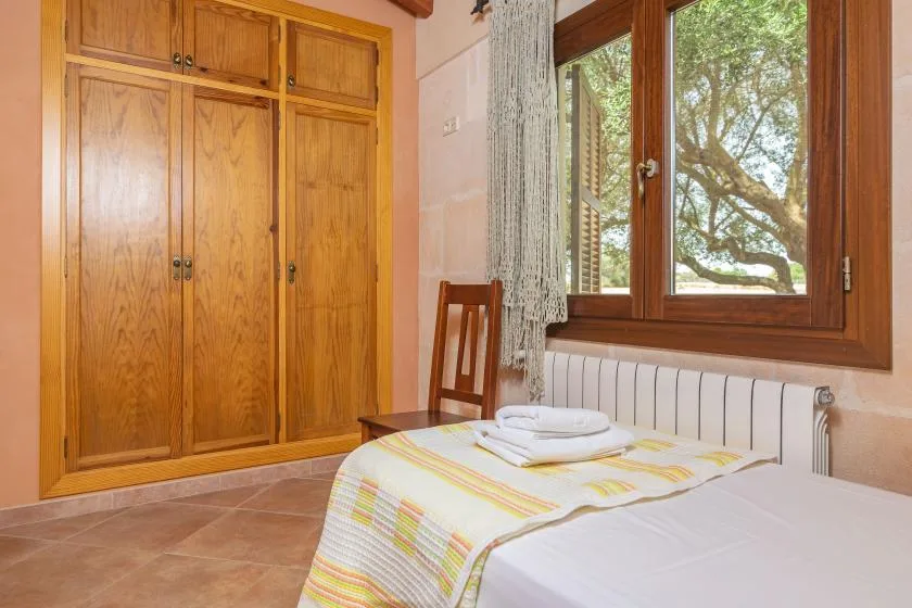 A bedroom with a bed beside a wooden wardrobe and a window.