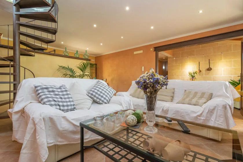 A living room with white seating, a glass coffee table, and a spiral staircase.