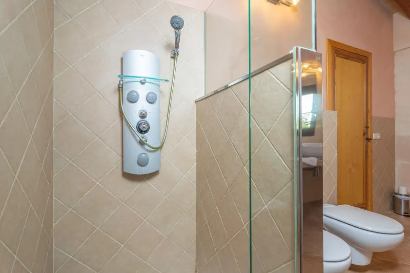 A tiled bathroom with a wall-mounted shower and glass partition.
