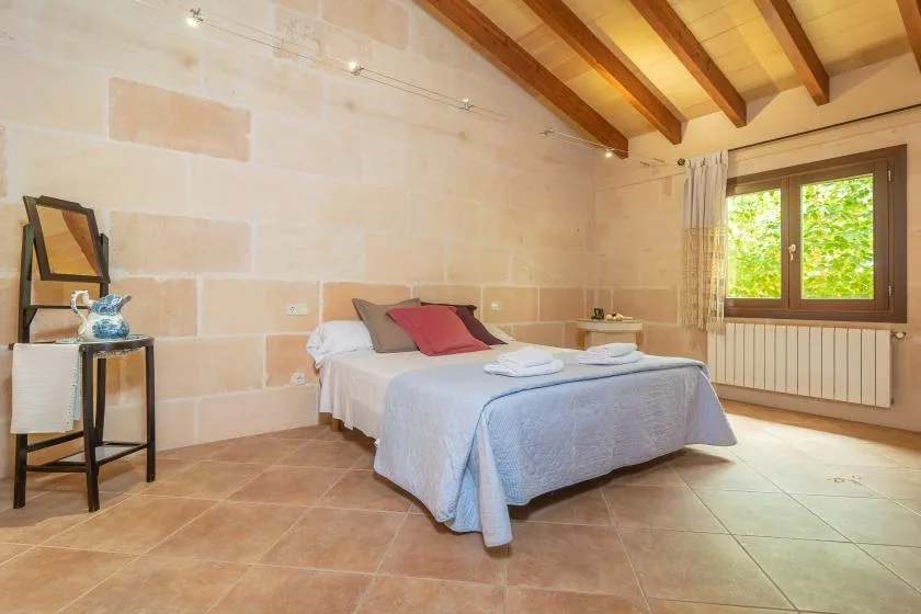 A bedroom with a bed, folded towels, and a window overlooking green foliage.