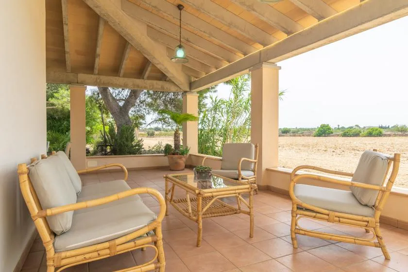 A covered patio with cushioned seating and a low table overlooks an open field.