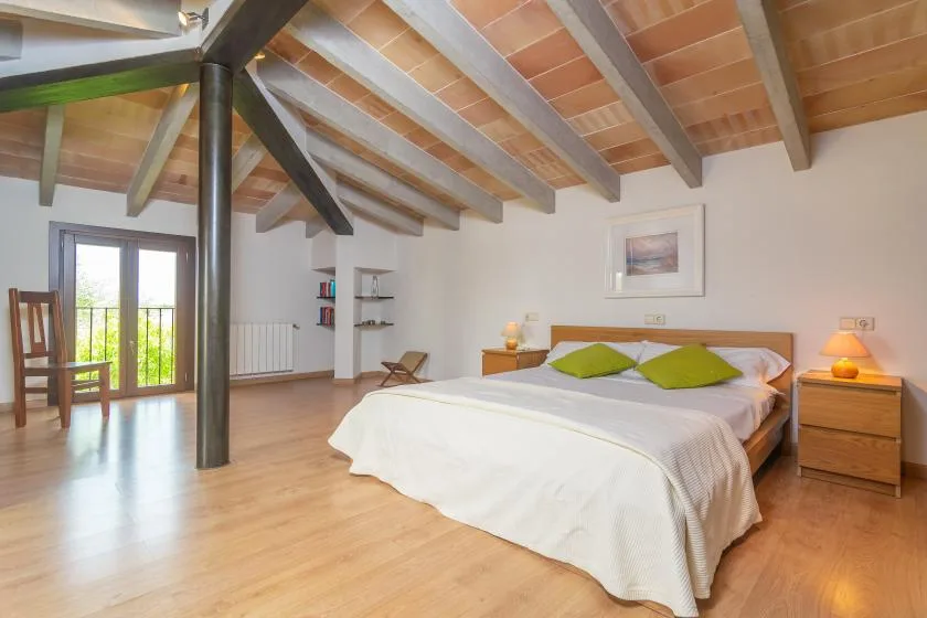 A bedroom with a double bed beneath a sloped, exposed-beam ceiling.